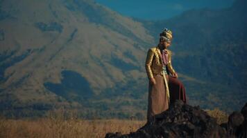 Man in traditional attire standing against mountain backdrop. video