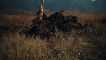 Traditional man standing on rocky terrain with mountains in the background during dusk. video