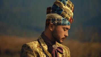 retrato de un hombre en tradicional étnico atuendo con un decorativo turbante, posando con un sereno expresión en contra un borroso natural antecedentes. video