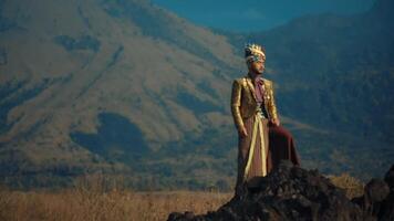 Man in traditional attire sitting on a rock with mountains in the background video