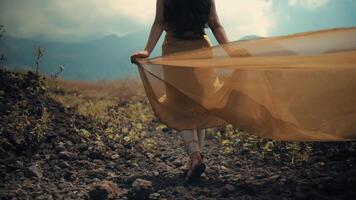 Woman in flowing dress walking in field with mountains in background. video