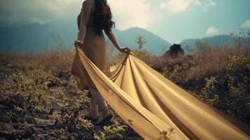 Woman in a flowing dress walking in a field with mountains in the background, evoking a sense of adventure and freedom. video