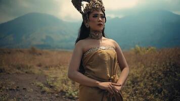 Elegant woman in traditional attire with a golden crown, posing in a field with mountains video