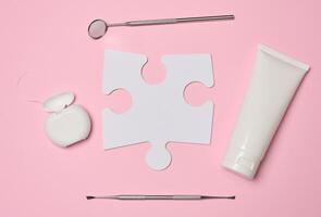 White tube with toothpaste, dental floss and paper puzzle on a pink background photo