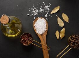 Salt, allspice, peppercorns and olive oil in a bottle on a black table photo