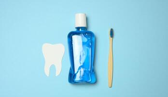 Plastic bottle with mouthwash, wooden toothbrush on blue background photo