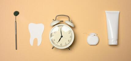 Alarm clock, tube of toothpaste and paper tooth on brown background, oral hygiene care photo