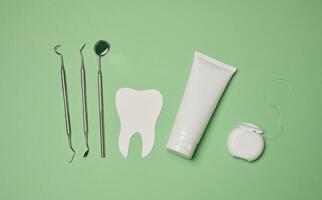 Tube with toothpaste, dental floss and medical mirror on a green background, oral hygiene. photo