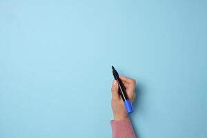A woman's hand holds a blue felt-tip pen on a blue background, space for an inscription photo