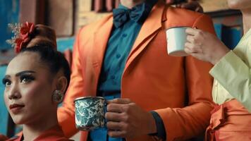 Three people in colorful attire holding mugs, partial faces visible, suggesting a casual social gathering or coffee break. video