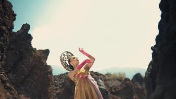 Woman in vibrant costume dancing between rocks under a cloudy sky. video