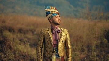 Man in traditional attire with headdress standing in a field, looking into the distance. video