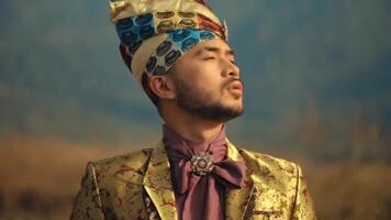 Man in traditional attire with a patterned turban, looking pensive against a blurred natural background. video