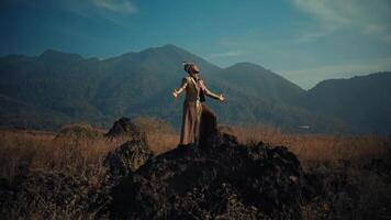 homme dans élégant robe permanent sur rocheux terrain avec montagnes dans le arrière-plan, bras tendu, embrassement la nature. video