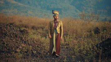 Traditional man in ethnic attire standing in a rugged field with mountains in the background at dusk. video