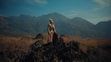 man in vintage dress standing in a field with mountains in the background. video