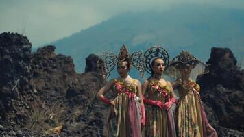 Three women in traditional attire with ornate headdresses standing before a mountainous backdrop. video