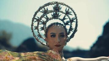 Woman with avant-garde headpiece and makeup posing in a dramatic outdoor setting. video