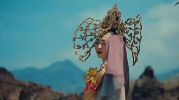 Elegant woman in traditional costume with ornate headdress against mountainous backdrop. video