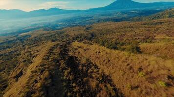 aérien vue de une vaste, ensoleillé paysage avec roulant collines et une loin Montagne en dessous de une clair ciel. video