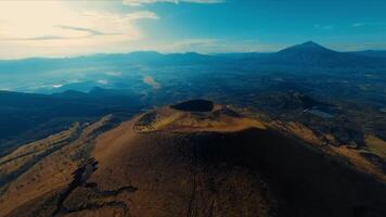 aérien vue de une volcanique paysage avec une important cratère et loin Montagne en dessous de une clair ciel. video