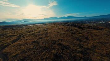 Aerial view of a vast, dry grassland with distant mountains under a clear blue sky. video