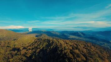 aérien vue de une luxuriant Montagne intervalle en dessous de une clair bleu ciel avec vaporeux des nuages. video