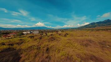 panorâmico Visão do uma exuberante campo com espalhados casas debaixo uma azul céu com fofo nuvens. video