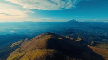 Antenne Aussicht von ein bergig Landschaft mit ein prominent Gipfel unter ein Blau Himmel mit wispy Wolken. video
