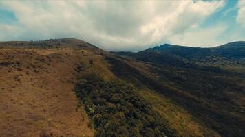 panoramico aereo Visualizza di rotolamento colline con lussureggiante verdura sotto un' drammatico nuvoloso cielo. video