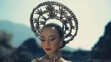 Woman with avant-garde headpiece and makeup posing in a dramatic outdoor setting. video