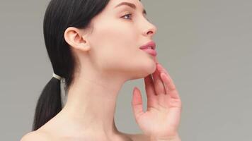 Close up beauty portrait of young woman with smooth healthy skin, she gently touches her face with her fingers on light grey background and smiles video