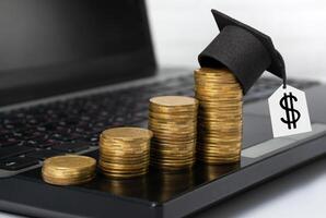 Concept of financial literacy and education. Gold coins with graduation hat stand on laptop on desktop photo