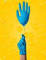 Cleaning concept. A hand in a blue glove holds a ball in the form of a glove on a yellow background. Spring cleaning. photo