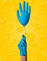 Cleaning concept. A hand in a blue glove holds a ball in the form of a glove on a yellow background. Spring cleaning. photo