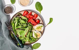 Ketogenic food. Boiled eggs, strawberries and fresh salad sprinkled with sesame seeds and chia seeds. Healthy food. Hard light. White background. View from above. Copy space. photo