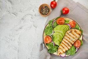 Grilled chicken breast and fresh vegetable salad with spinach leaves, avocado and tomatoes on a light background. Salad of greens with meat. The concept of diet food. Copy space. Food banner. photo