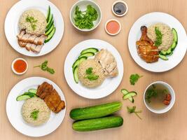 Chicken Cutlet and Roast Pork Rice, Roast Pork, Roasted Chicken, Roast Pork, Steamed Chicken with raw cucumber, Coriander, salad, sauce and soup served in a dish isolated on wooden background top view photo