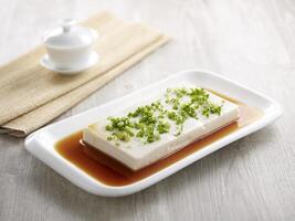 Steamed Spring Water Tofu in Supreme Soya Sauce with chopsticks served in a dish isolated on mat side view on grey background photo