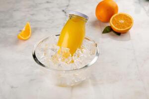 A bottle of FRESH ORANGE JUICE served in iced cube bowl side view on grey background photo