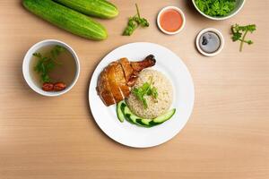 Roasted Chicken rice with raw cucumber, Coriander, salad, sauce and soup served in a dish isolated on wooden background top view photo