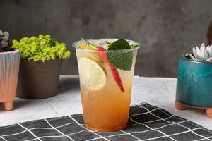 Thai iced red chili lemonade served in disposable glass with ice cube isolated on wooden board side view of taiwanese ice drink photo