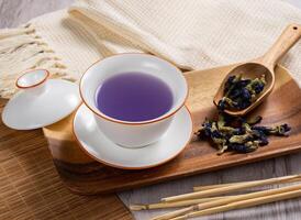 A cup butterfly pea coconut water on wooden dish with raw butterfly followers on wooden spoon photo