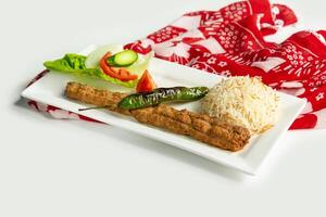 Turkish style adana kebab with rice and salad in a dish isolated on colorful table cloth side view on grey background photo