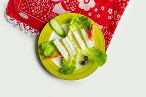 Traditional Turkish Cheese or Beyaz Peynir with cucumber and tomato in a dish isolated on colorful table cloth top view on grey background photo