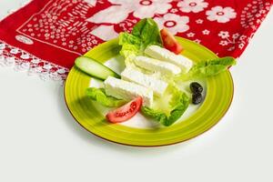 Traditional Turkish Cheese or Beyaz Peynir with cucumber and tomato in a dish isolated on colorful table cloth top view on grey background photo