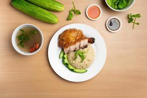 Roasted Chicken and Roast Pork Rice with raw cucumber, Coriander, salad, sauce and soup served in a dish isolated on wooden background top view photo