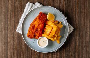 Traditional fried Fish and chips with tartar sauce in white plate on dark wooden background top view photo