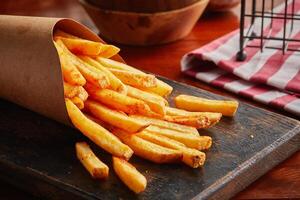 French Fries served in a wooden board isolated on wooden background side view photo