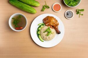 Roasted Chicken rice with raw cucumber, Coriander, salad, sauce and soup served in a dish isolated on wooden background top view photo
